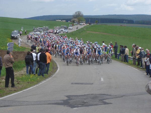Un grand peloton de cyclistes sur la route qui longe la maison.