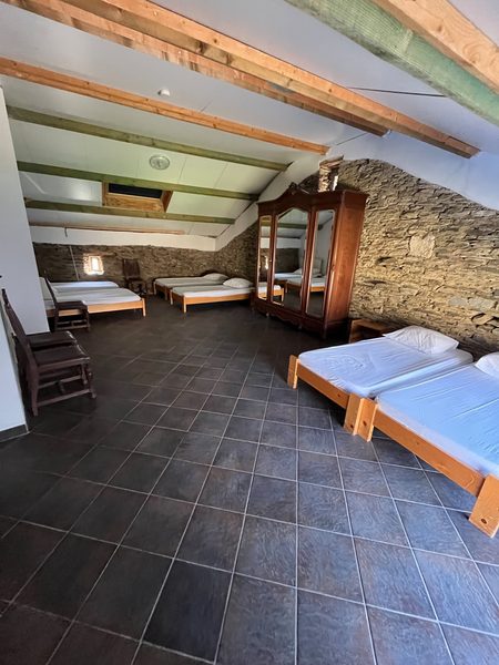 Un dortoir avec des lits sous le plafond à poutres, contre le mur en pierre.